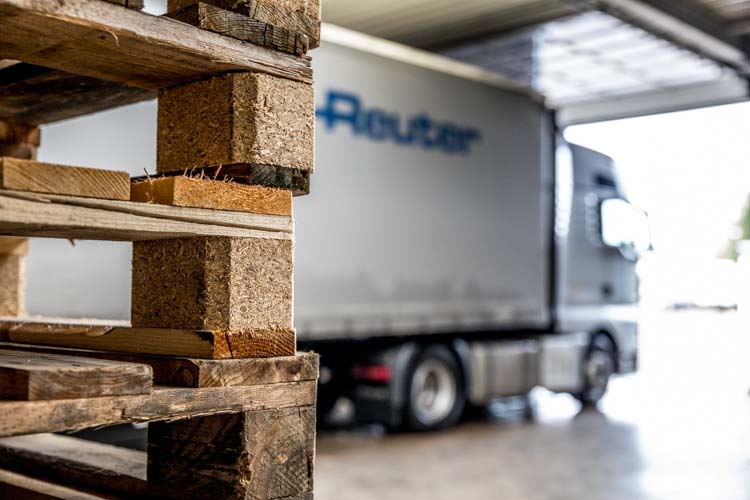 Blick auf einen LKW in der Halle von Spedition Reuter, der hinter einem Stapel Holz-Paletten steht.
